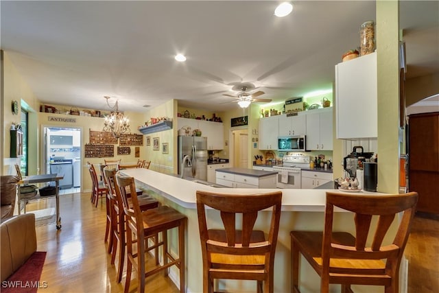 kitchen with white cabinets, kitchen peninsula, stainless steel appliances, and hanging light fixtures