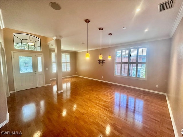 foyer entrance featuring plenty of natural light, wood finished floors, ornate columns, and ornamental molding