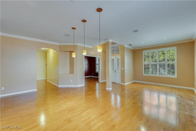 unfurnished living room with baseboards, arched walkways, light wood finished floors, and ornamental molding