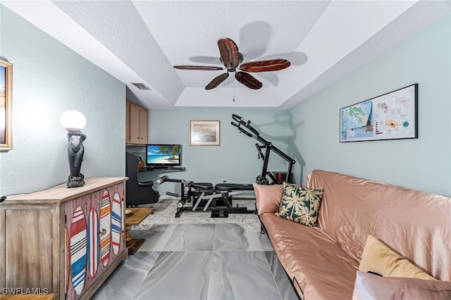 living room with a tray ceiling, ceiling fan, and a textured ceiling