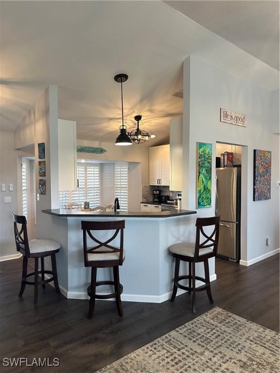 kitchen with stainless steel refrigerator, kitchen peninsula, white cabinetry, and dark hardwood / wood-style flooring