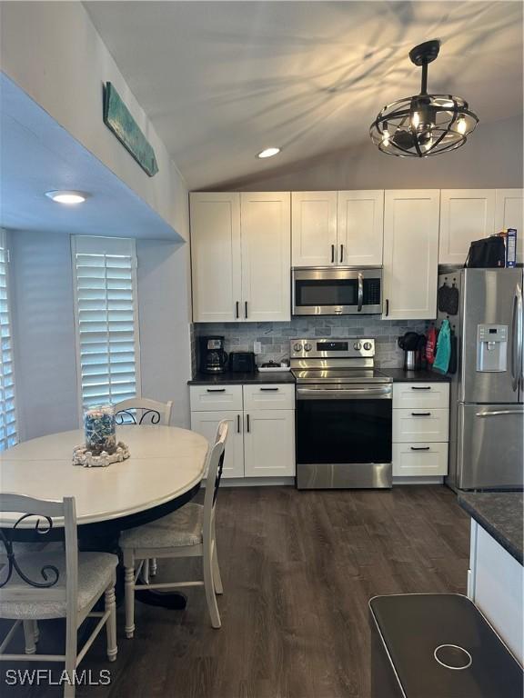 kitchen with hanging light fixtures, vaulted ceiling, decorative backsplash, white cabinets, and appliances with stainless steel finishes