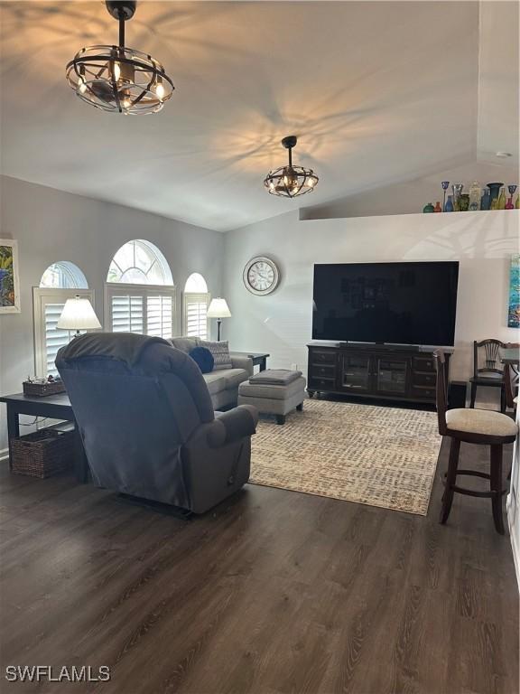 living room with a notable chandelier, dark hardwood / wood-style floors, and vaulted ceiling