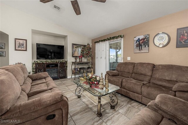 living area featuring a glass covered fireplace, lofted ceiling, a ceiling fan, and visible vents