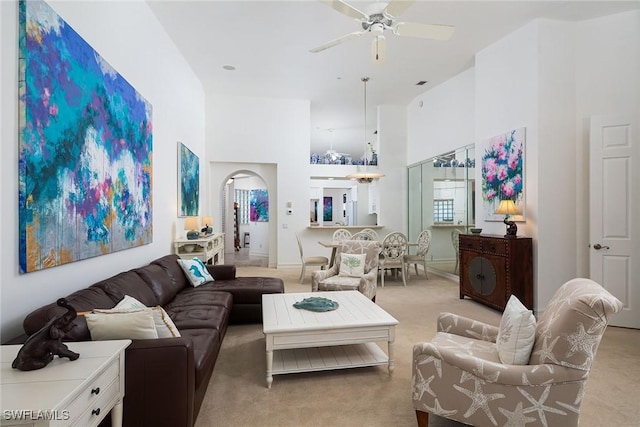 carpeted living room with ceiling fan and a high ceiling