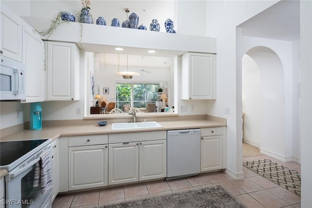 kitchen with white appliances, sink, ceiling fan, light tile patterned floors, and white cabinetry