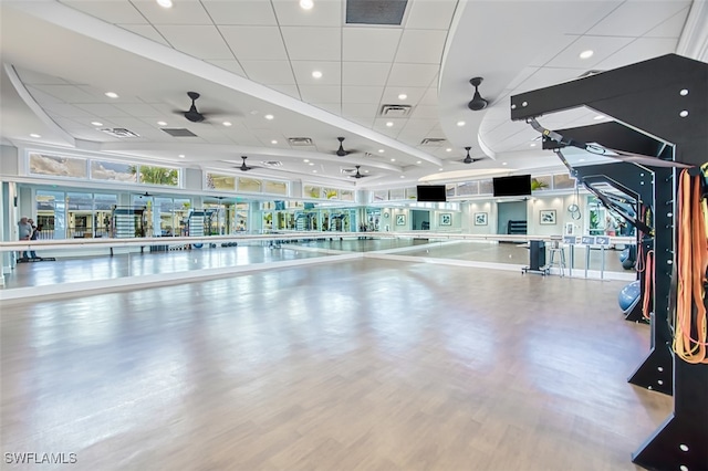 workout area featuring ceiling fan, a drop ceiling, and a wall of windows