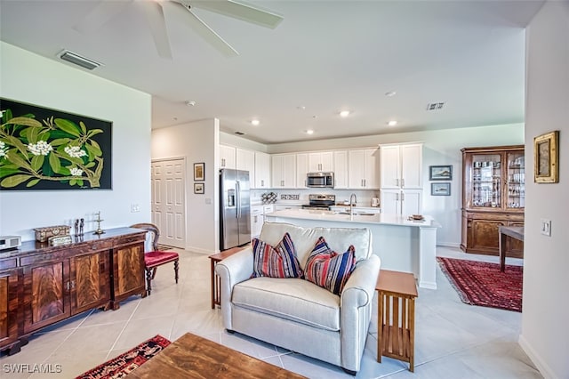 kitchen with sink, light tile patterned floors, appliances with stainless steel finishes, white cabinets, and a center island with sink