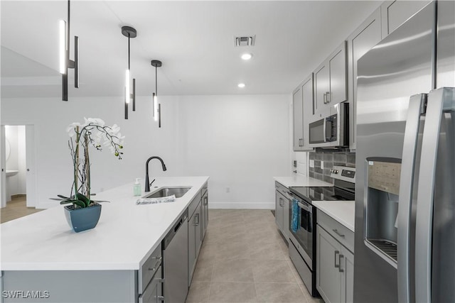 kitchen featuring gray cabinetry, sink, decorative light fixtures, a kitchen island with sink, and appliances with stainless steel finishes