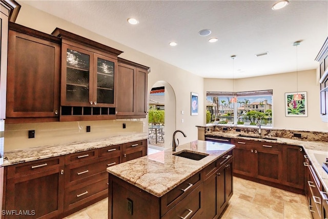 kitchen featuring pendant lighting, an island with sink, light stone counters, and sink