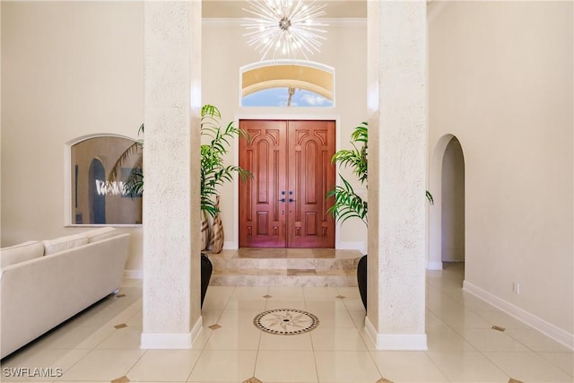 tiled foyer featuring a notable chandelier, crown molding, and a high ceiling