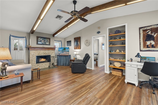 interior space with lofted ceiling, built in shelves, a stone fireplace, ceiling fan, and hardwood / wood-style flooring