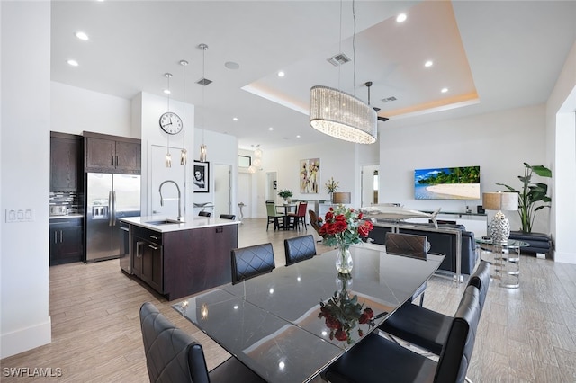 dining room featuring a raised ceiling, sink, an inviting chandelier, and light hardwood / wood-style flooring