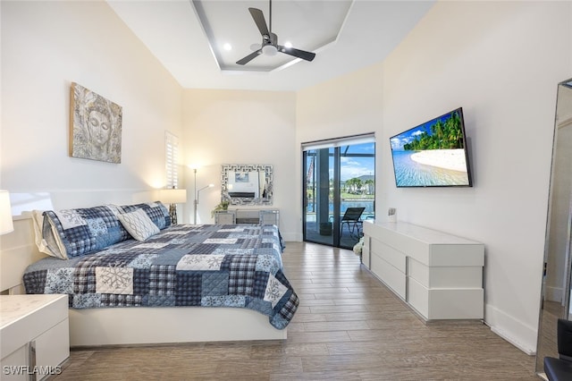 bedroom featuring access to exterior, light hardwood / wood-style flooring, a raised ceiling, and ceiling fan