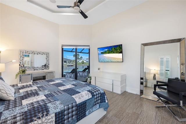 bedroom featuring access to exterior, light hardwood / wood-style floors, a raised ceiling, and ceiling fan