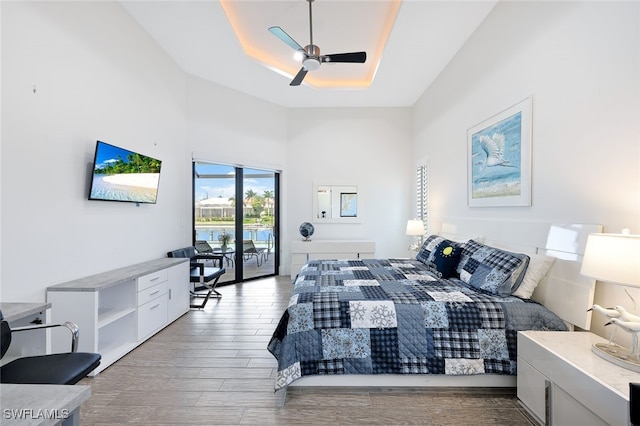 bedroom featuring a tray ceiling, access to outside, light hardwood / wood-style floors, and ceiling fan