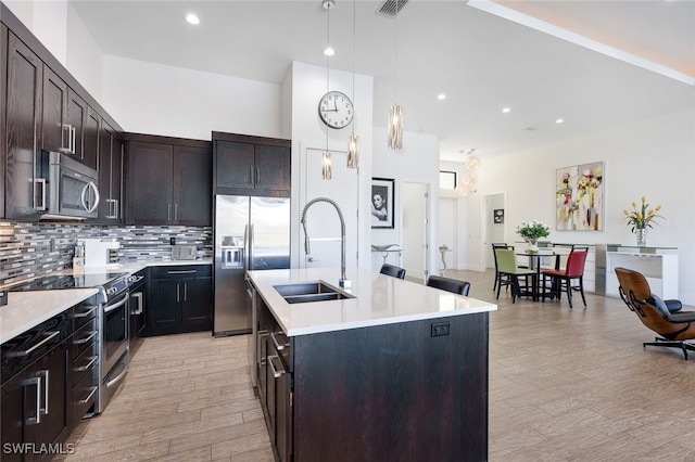 kitchen featuring an island with sink, appliances with stainless steel finishes, sink, and light wood-type flooring