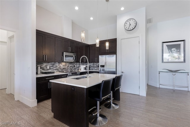 kitchen featuring a kitchen bar, sink, appliances with stainless steel finishes, pendant lighting, and a kitchen island with sink