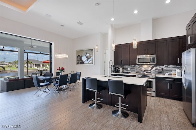 kitchen featuring a breakfast bar, hanging light fixtures, a center island with sink, stainless steel appliances, and decorative backsplash