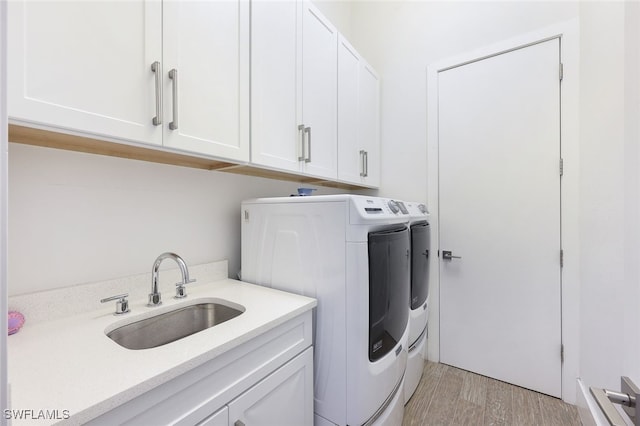 clothes washing area with cabinets, washer and dryer, sink, and light hardwood / wood-style floors