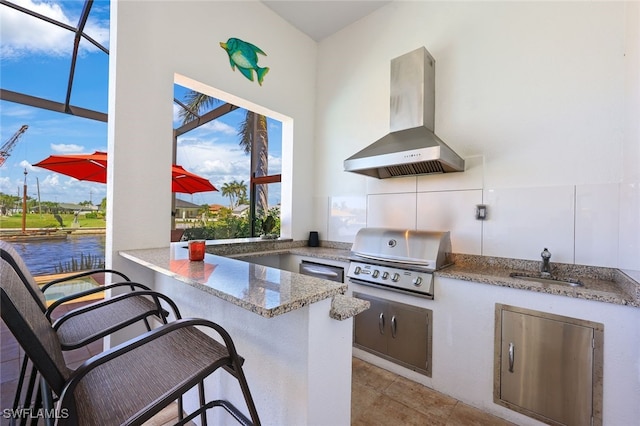 kitchen with sink, a kitchen breakfast bar, light stone counters, kitchen peninsula, and wall chimney exhaust hood