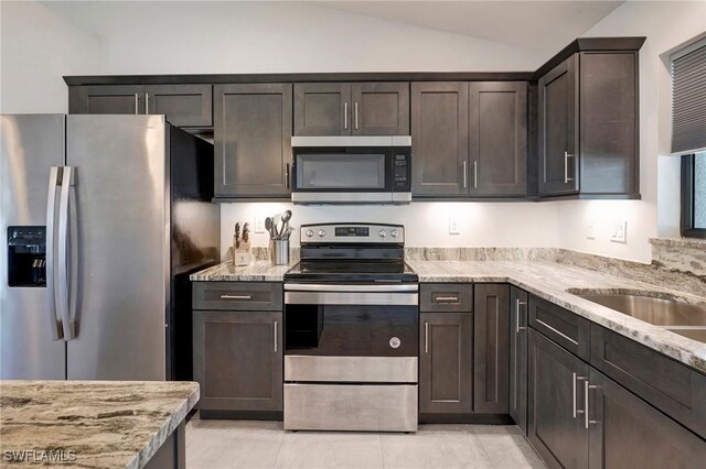 kitchen featuring lofted ceiling, light tile patterned floors, light stone counters, dark brown cabinetry, and stainless steel appliances