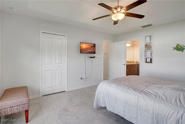 bedroom with a closet, ensuite bathroom, ceiling fan, and a tray ceiling