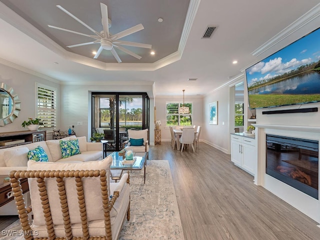 living room featuring a tray ceiling, ceiling fan, crown molding, and light hardwood / wood-style floors