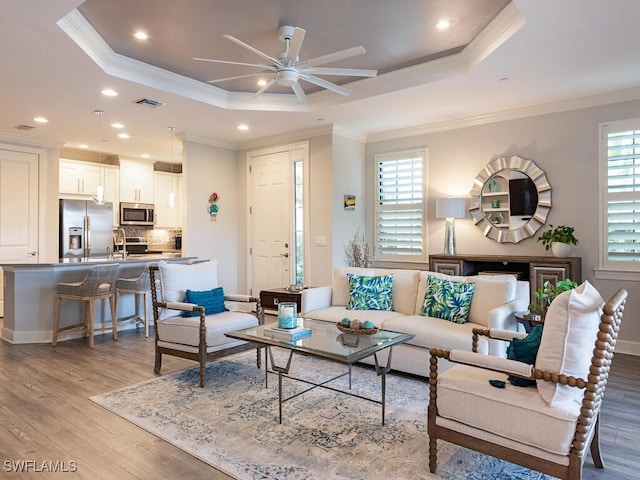 living room featuring a tray ceiling, ceiling fan, light wood-type flooring, and ornamental molding