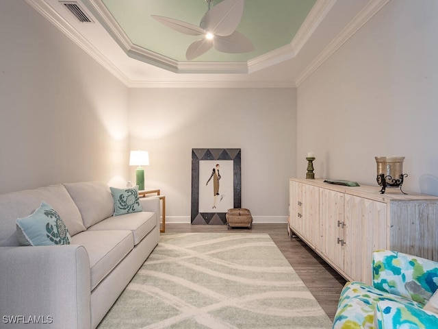 living room featuring a raised ceiling, ceiling fan, crown molding, and hardwood / wood-style flooring