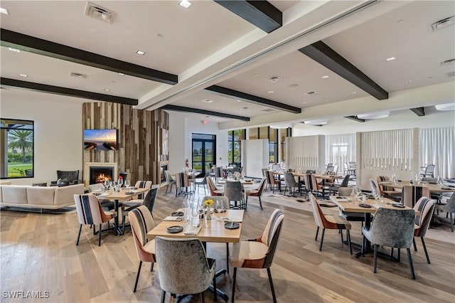 dining area featuring a large fireplace, beamed ceiling, and light hardwood / wood-style flooring