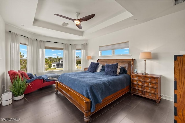 bedroom featuring multiple windows, a tray ceiling, dark hardwood / wood-style floors, and ceiling fan