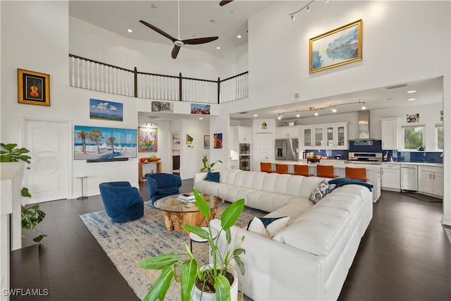 living room with ceiling fan, dark hardwood / wood-style flooring, and a high ceiling