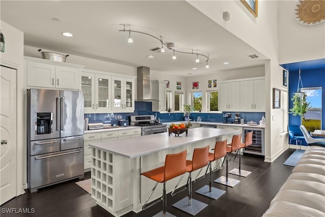 kitchen featuring appliances with stainless steel finishes, white cabinetry, wine cooler, a center island, and wall chimney exhaust hood