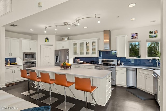 kitchen with appliances with stainless steel finishes, white cabinetry, a center island, decorative backsplash, and wall chimney exhaust hood