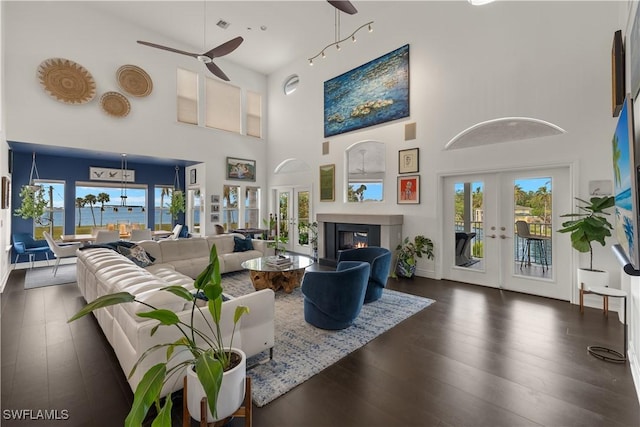 living room with a water view, a towering ceiling, ceiling fan, and french doors