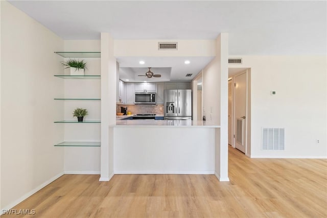 kitchen with kitchen peninsula, decorative backsplash, light wood-type flooring, and appliances with stainless steel finishes