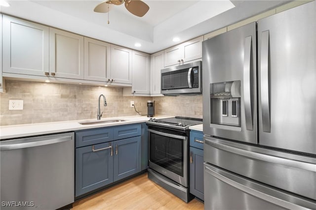 kitchen featuring appliances with stainless steel finishes, tasteful backsplash, ceiling fan, sink, and light hardwood / wood-style floors