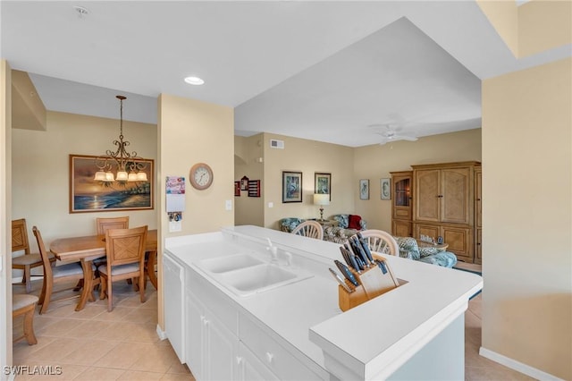 kitchen with sink, white cabinets, pendant lighting, light tile patterned flooring, and ceiling fan with notable chandelier