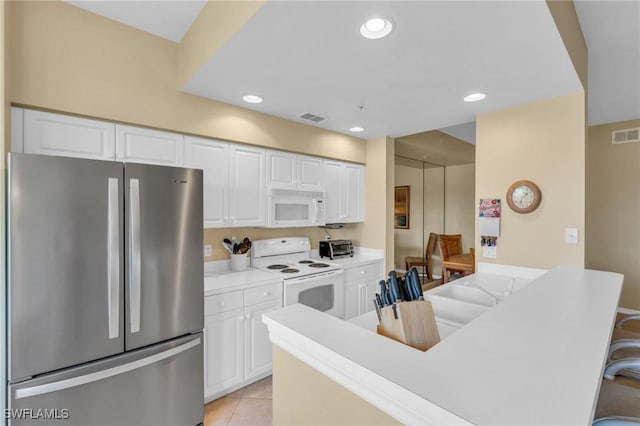 kitchen with a breakfast bar, white appliances, white cabinets, light tile patterned floors, and kitchen peninsula