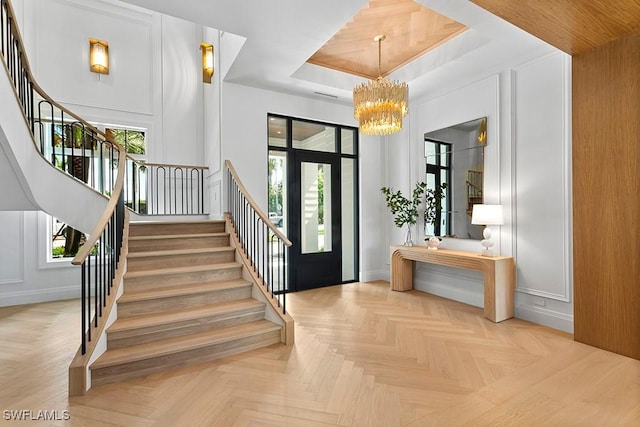 foyer with a tray ceiling, light parquet floors, and a notable chandelier