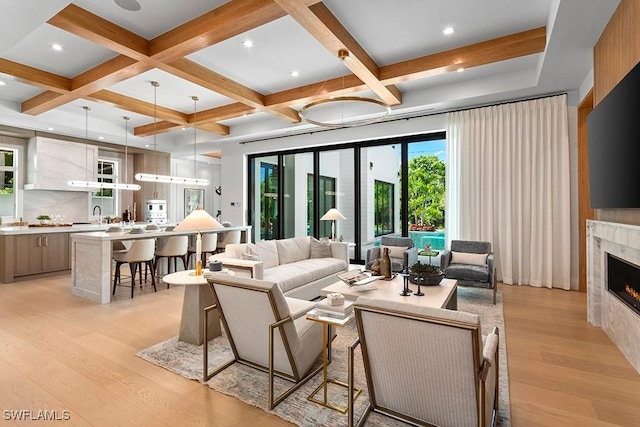 living room featuring beamed ceiling, a high end fireplace, light hardwood / wood-style floors, and coffered ceiling