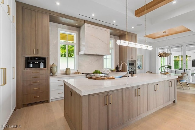 kitchen featuring light stone counters, custom exhaust hood, pendant lighting, a center island with sink, and white cabinetry