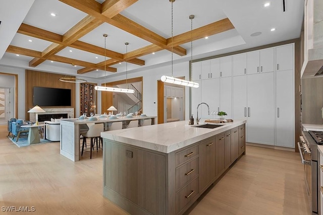 kitchen featuring pendant lighting, a large island with sink, coffered ceiling, and sink