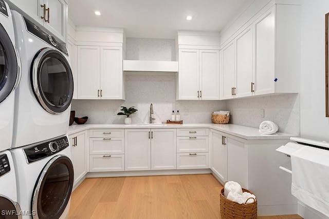 clothes washing area with cabinets, sink, washing machine and dryer, stacked washing maching and dryer, and light wood-type flooring