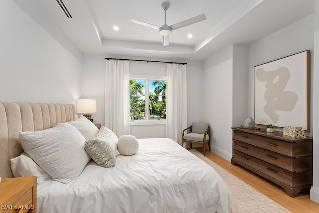 bedroom with ceiling fan, light wood-type flooring, and a tray ceiling