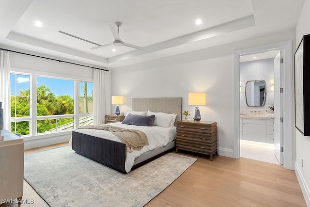 bedroom featuring a raised ceiling, ensuite bath, and ceiling fan