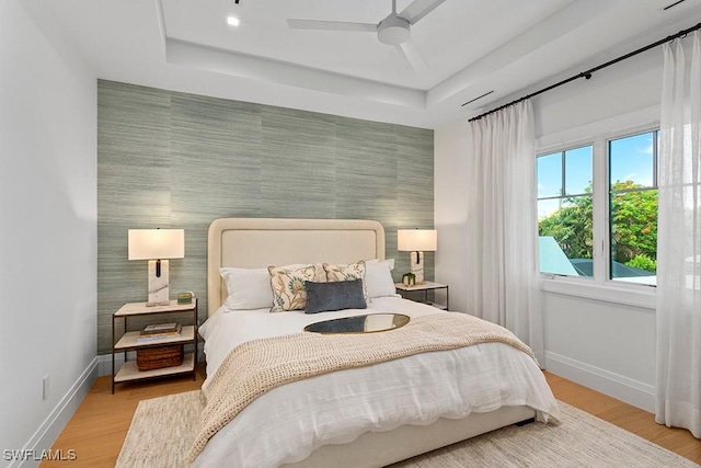 bedroom featuring a tray ceiling, ceiling fan, and light hardwood / wood-style floors