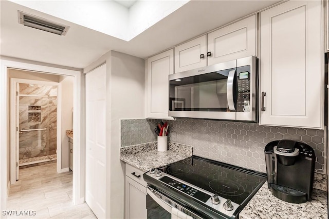 kitchen with decorative backsplash, light stone countertops, white cabinetry, and appliances with stainless steel finishes