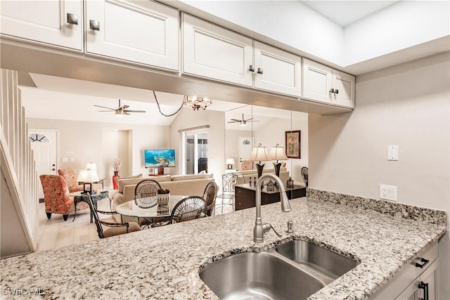 kitchen with white cabinets, ceiling fan, light stone countertops, and sink